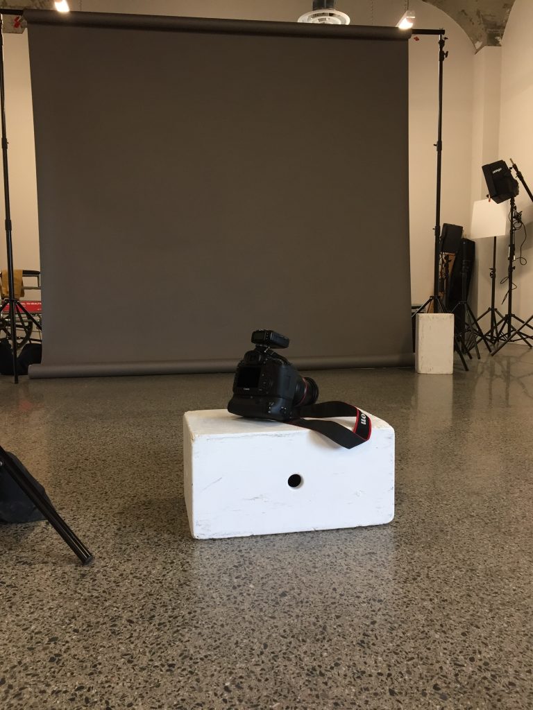 Image of camera on an apple box in front of a grey screen in a photography studio.
