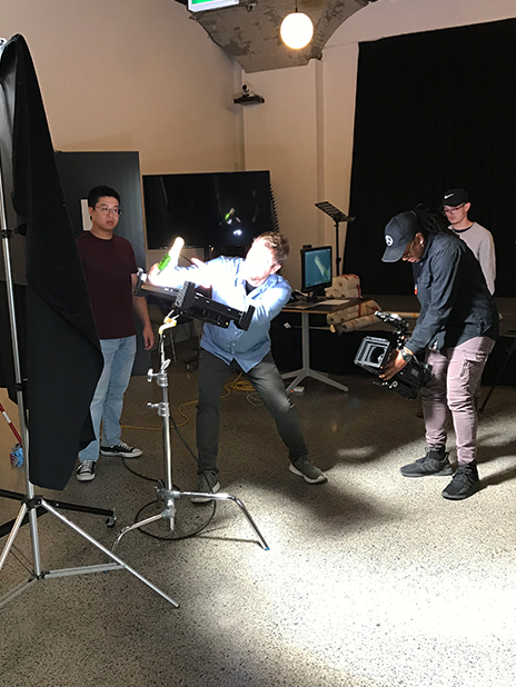 Four crew with video camera and lights filming a Champagne bottle in a video studio.