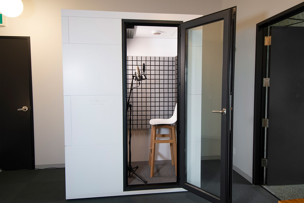 A soundproof audio booth, door open, with a stool and microphone