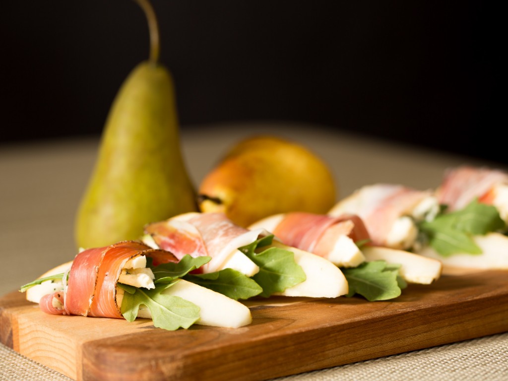 Pear wrapped in prosciutto on a wooden board